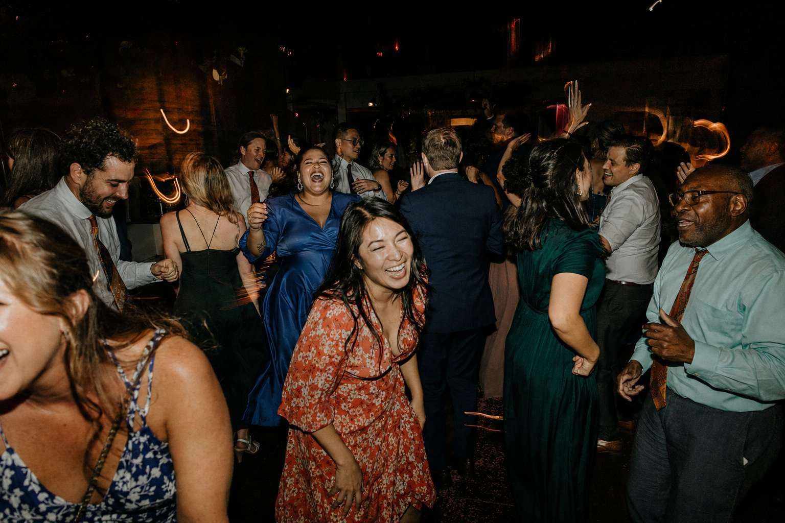 Wedding guests laughing and dancing together on a packed evening dance floor